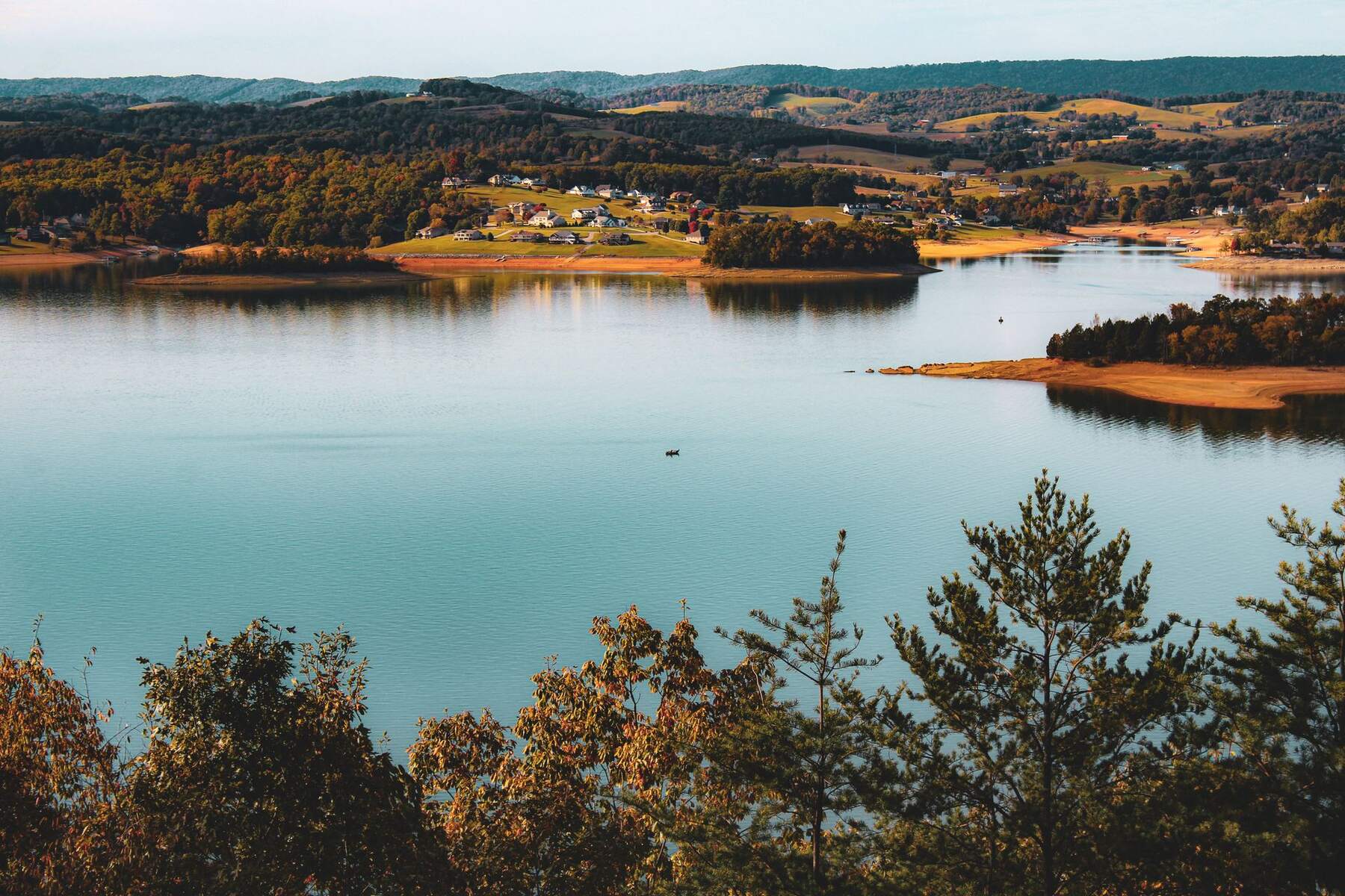 Calm blue-green lake with a wooded, autumn-colored shoreline and a lakeside community visible on a point