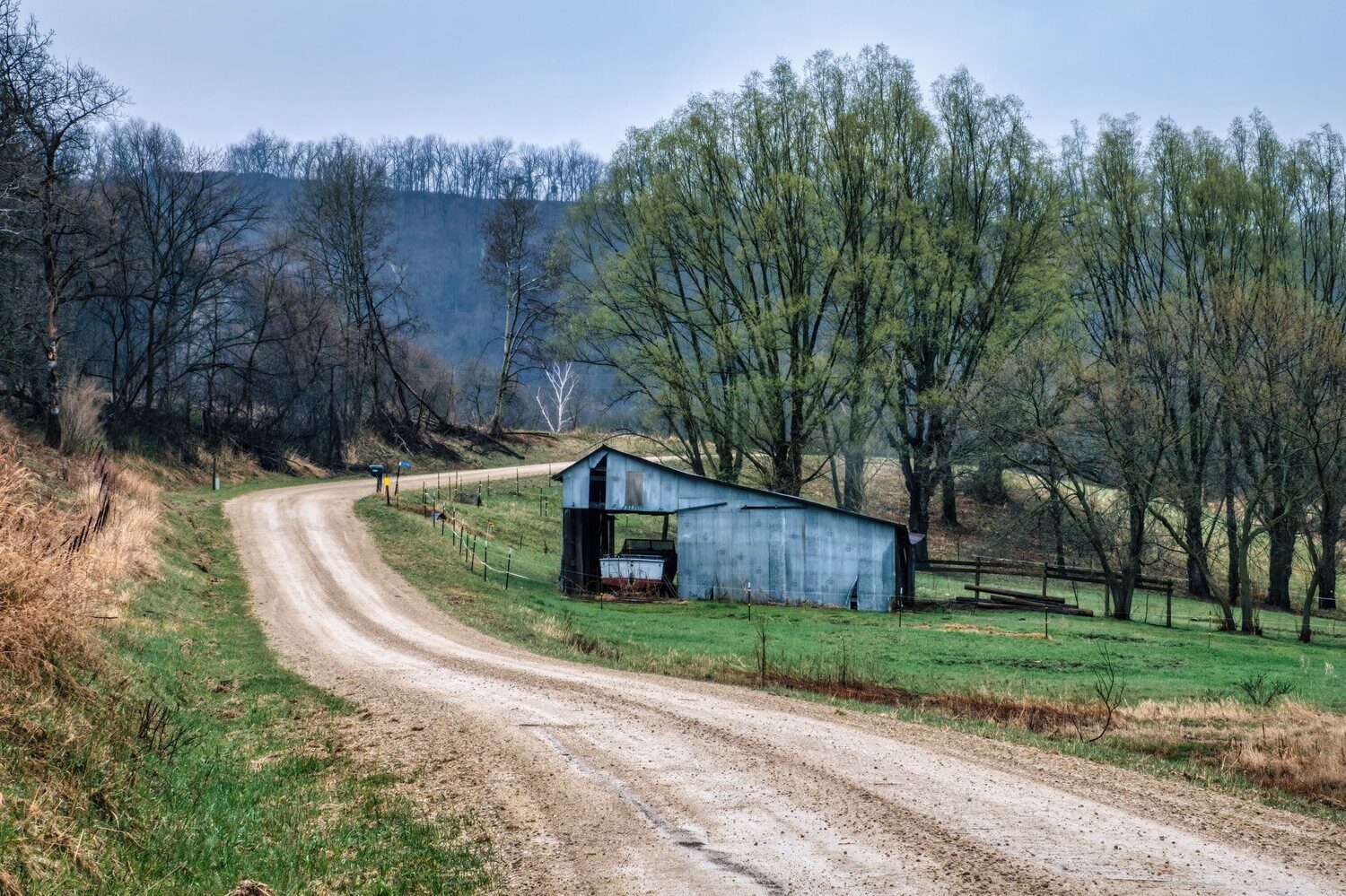A gravel country road passing a weathered barn in open countryside